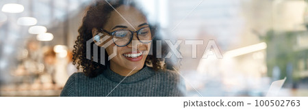 Smiling woman freelancer working laptop and making notes while sitting near windows in cozy cafe 100502763