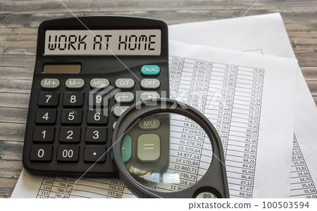 The text Work at Home on the display of a calculator on top of the office table, which lies The text Work at Home on the display of a calculator on top of the office table, which lies 100503594