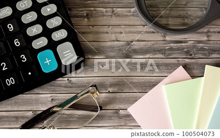 On a wooden background magnifier, calculator, notepad On a wooden background magnifier, calculator, notepad 100504073