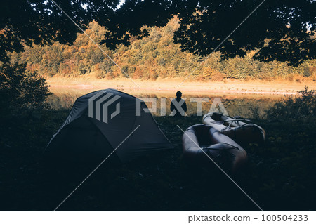 Man near his tent and packrafts in forest camp Man near his tent and packrafts in forest camp 100504233