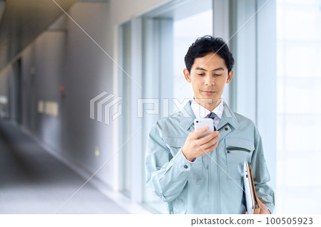 一位穿著工作服的工程師在辦公室走廊裡操作智能手機 一位穿著工作服的工程師在辦公室走廊裡操作智能手機 100505923