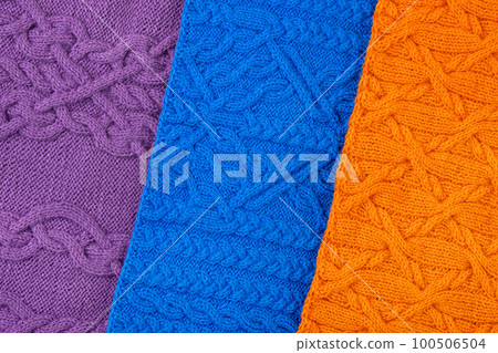 Knitted blue, lilac and orange background. Large knitted fabric with a pattern. Close-up of a knitted blanket. Banner 100506504