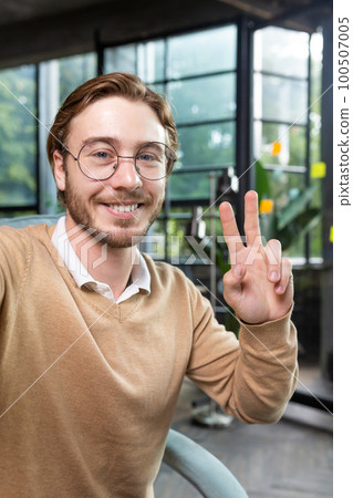 Close-up photo. Portrait of professional smart male programmer hacker taking selfie with hand, showing victory gesture with fingers. Smiles into the phone camera. Close-up photo. Portrait of professional smart male programmer hacker taking selfie with hand, showing victory gesture with fingers. Smiles into the phone camera. 100507005