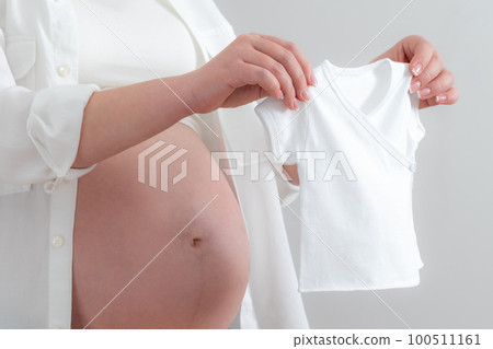 Pregnant woman holding little baby clothes, concept of expecting baby 100511161