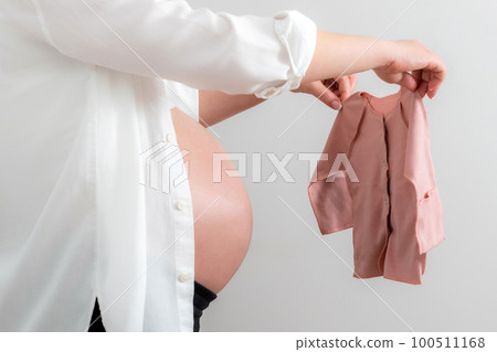 Pregnant woman holding baby clothes as a concept of expecting a baby 100511168