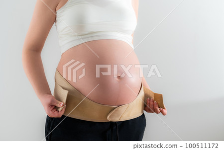 Pregnant woman adjusts additional fasteners on the orthopedic belt to support the belly Pregnant woman adjusts additional fasteners on the orthopedic belt to support the belly 100511172