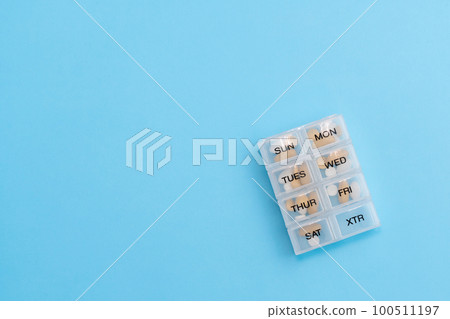 Pill organizer with variety of pills and supplement. Weekly Pill container on blue background with copy space 100511197
