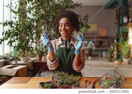 Smiling woman florist wearing apron examines seedlings in floral studio. Gardening concept 100511960