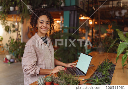 Successful female florist working laptop in own floral studio, check customers order  100511961