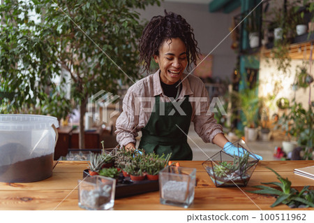 Happy smiling woman florist making succulent plant composition at floral design studio 100511962