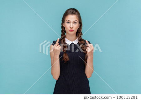 Portrait of serious vulgar woman with braids showing middle finger, impolite gesture disrespects someone looks rude at camera, wearing black dress. woman Indoor studio shot isolated on blue background 100515291