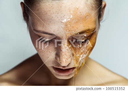 Closeup portrait of adorable winsome young brunette woman with freckles and honey mask, standing with closed eyes or looking down. Indoor studio shot isolated on gray background. Closeup portrait of adorable winsome young brunette woman with freckles and honey mask, standing with closed eyes or looking down. Indoor studio shot isolated on gray background. 100515352