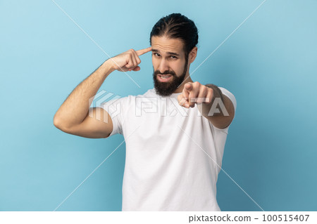 You are nuts. Portrait of man with beard showing stupid gesture and pointing to camera, accusing dumb insane suggestion, crazy plan for idiots. Indoor studio shot isolated on blue background. You are nuts. Portrait of man with beard showing stupid gesture and pointing to camera, accusing dumb insane suggestion, crazy plan for idiots. Indoor studio shot isolated on blue background. 100515407