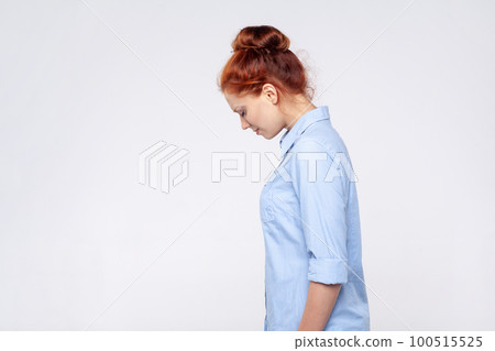 Side view portrait of sad upset redhead woman wearing blue shirt crying with sorrow, feeling lonely hopeless, desperate emotions, worried about troubles. Indoor studio shot isolated on gray background 100515525