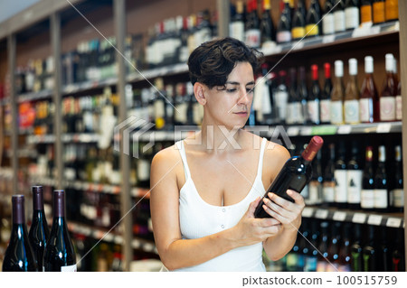 Young brunette visiting winehouse in search of bottle of wine Young brunette visiting winehouse in search of bottle of wine 100515759
