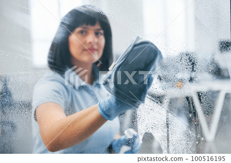 Woman cleaning dirty window by using towel. View through the glass 100516195