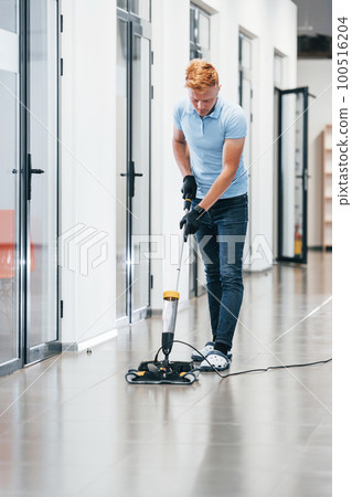 Young man works in the modern office. Uses vacuum cleaner 100516204