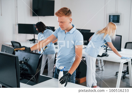 Cleans monitor. Group of workers clean modern office together at daytime 100516233
