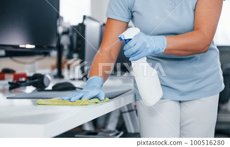 Close up view of woman in protective gloves that cleaning tables in the office 100516280