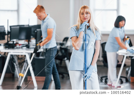 Cleans floor. Group of workers clean modern office together at daytime Cleans floor. Group of workers clean modern office together at daytime 100516402