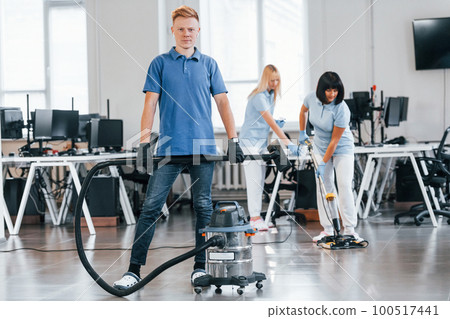Guy with vacuum cleaner. Group of workers clean modern office together at daytime 100517441