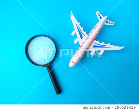 Magnifying glass and white toy airplane on a blue background. 100521429