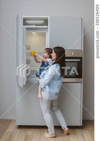 Mother holds a child in her arms and opens the refrigerator. 100526409