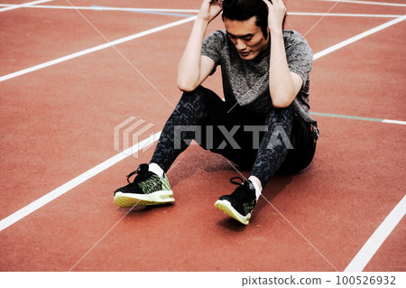 完成後坐在田徑跑道上的男賽跑者 完成後坐在田徑跑道上的男賽跑者 100526932