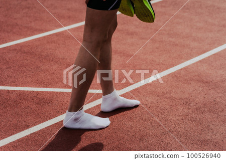 Male runner walking with shoes off after finish on athletics track 100526940