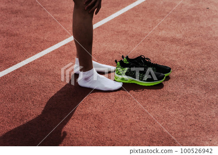 Male runner taking off shoes after finish on athletics track 100526942