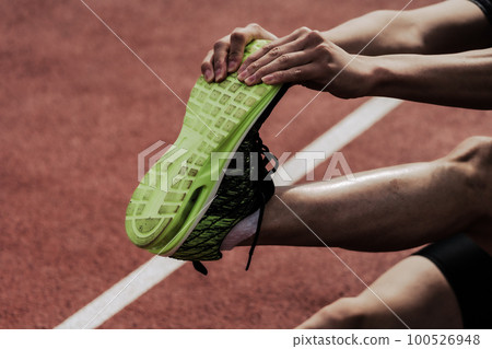 The lower body of a male runner stretching and caring for his legs on the track of an athletics stadium The lower body of a male runner stretching and caring for his legs on the track of an athletics stadium 100526948