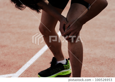 The lower body of a male runner who cares by holding his knees on the track of an athletics stadium 100526953