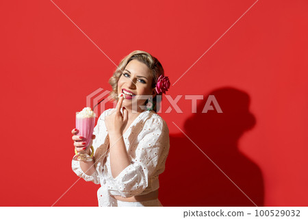 Woman drinking a milkshake against a red background. Retro style woman portrait 100529032