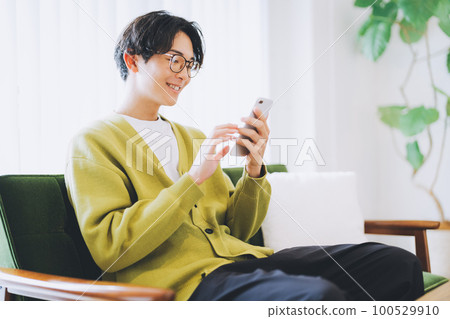 A man sitting on the couch and using a smartphone 100529910