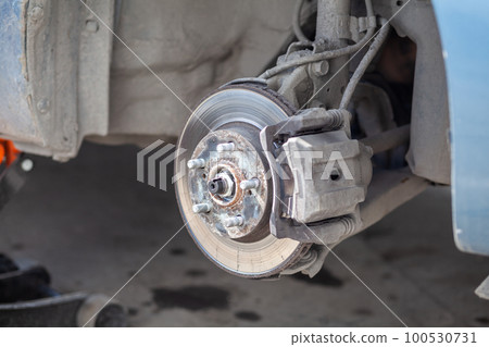 Disc brake of the vehicle for repair, in process of new tire replacement. Car brake repairing in garage.Suspension of car for maintenance brakes and shock absorber systems. Replacement of brake pads. 100530731