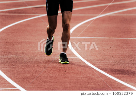 Runner running on athletics track 100532379