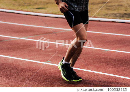 Male runner running straight on athletics track 100532385