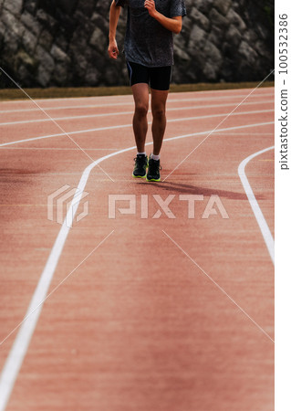 Male runner running straight on athletics track 100532386