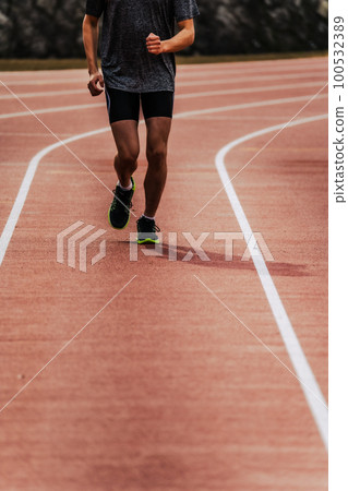 Male runner running straight on athletics track 100532389