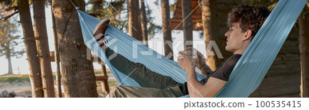 Handsome man having relax day in forest house. Sipping coffee in hammock in wood in morning. Handsome man having relax day in forest house. Sipping coffee in hammock in wood in morning. 100535415