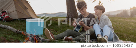 Cheerful couple of travelers sitting at fire in camp and man playing on guitar. Travel life Cheerful couple of travelers sitting at fire in camp and man playing on guitar. Travel life 100535427