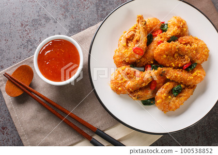 Asian style fried shrimp with salted egg yolks, curry leaves and chili served with chili sauce close-up in a plate. Horizontal top view Asian style fried shrimp with salted egg yolks, curry leaves and chili served with chili sauce close-up in a plate. Horizontal top view 100538852