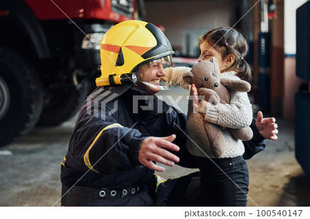Happy little girl is with male firefighter in protective uniform Happy little girl is with male firefighter in protective uniform 100540147