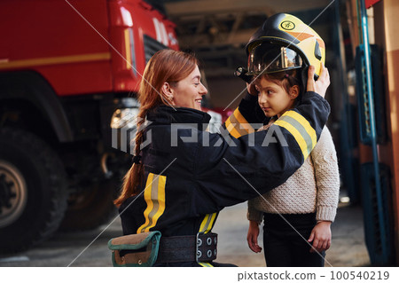 Happy little girl is with female firefighter in protective uniform Happy little girl is with female firefighter in protective uniform 100540219