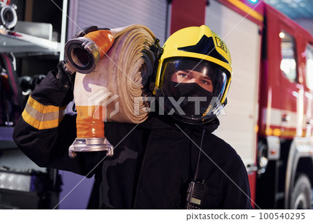 Holds hose. Male firefighter in protective uniform standing near truck Holds hose. Male firefighter in protective uniform standing near truck 100540295