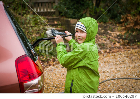 Happy child girl in waterproof clothes is helping parent washing car, water is splashing with sunlight Happy child girl in waterproof clothes is helping parent washing car, water is splashing with sunlight 100540297