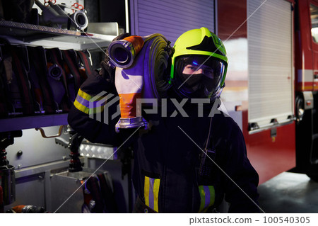Holds hose. Male firefighter in protective uniform standing near truck Holds hose. Male firefighter in protective uniform standing near truck 100540305