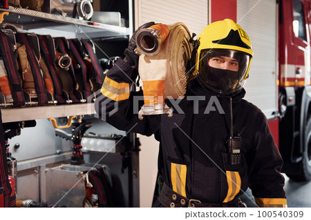 Holds hose. Male firefighter in protective uniform standing near truck Holds hose. Male firefighter in protective uniform standing near truck 100540309