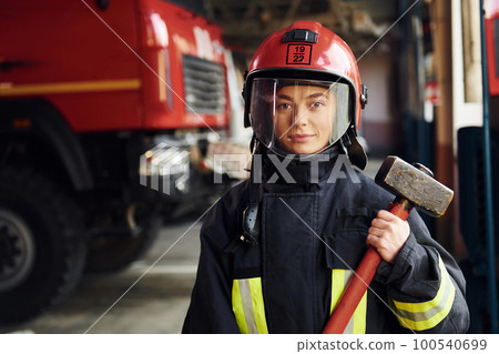 With hammer in hands. Female firefighter in protective uniform standing near truck 100540699