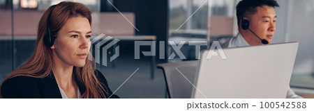 Businesswoman in headphones working on computer while sitting in modern office Businesswoman in headphones working on computer while sitting in modern office 100542588